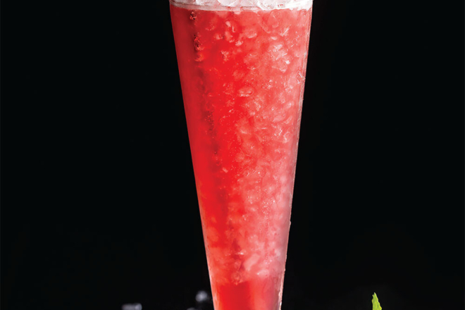 A red cocktail fills a trumpet glass with nugget ice accented by mint leaves