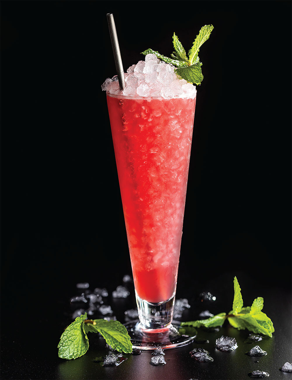 A red cocktail fills a trumpet glass with nugget ice accented by mint leaves