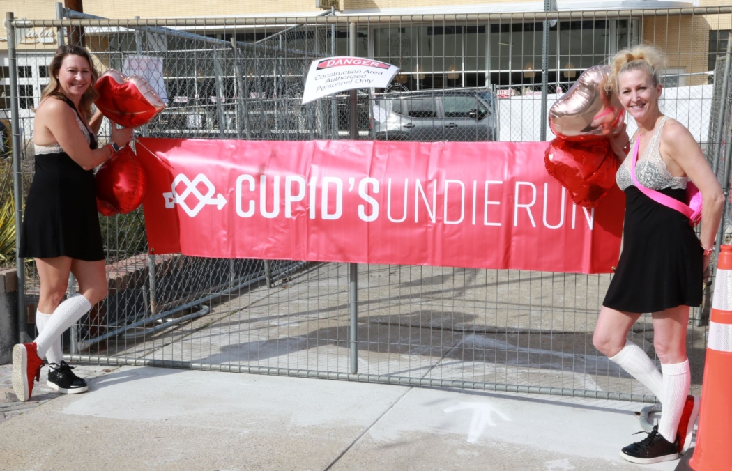 Two participants stand beside a red Cupid's Undie Run banner