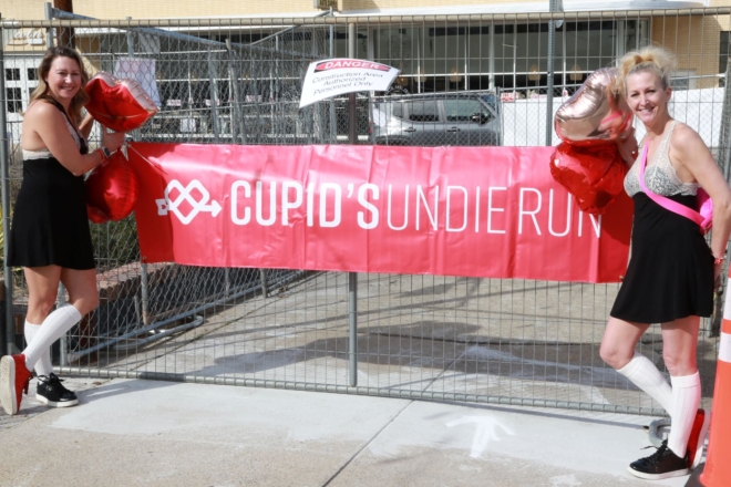 Two participants stand beside a red Cupid's Undie Run banner