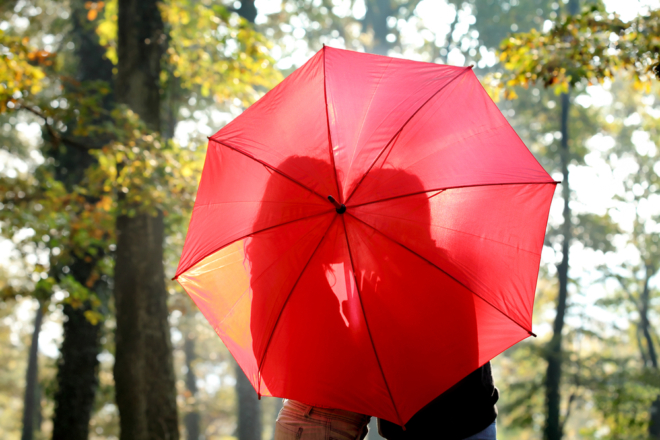 A couple kisses behind a red umbrella.